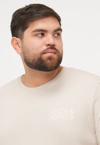 Beige katoenen t-shirt met een ronde hals en de tekst "JACK & JONES" subtiel in een tonale stijl gedrukt op de borst.