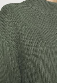 Sweter z dzianiny, ciemnozielony, prążkowana faktura, wysoki kołnierz, dopasowany fason, gładkie wykończenie, widoczne szwy, miękka tkanina.
