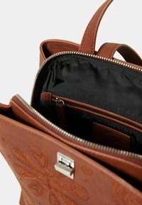Borsa in ecopelle marrone con stampa a rilievo, dotata di chiusura con zip, interiori neri e una piccola tasca con zip per l'organizzazione.