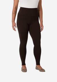 Leggings marroni a vita alta realizzati in un tessuto elastico e liscio. Presentano un design aderente e senza motivi o dettagli hardware visibili.