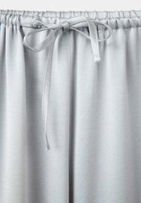 Pantalon gris clair avec une taille élastique et un cordon noué au centre devant.