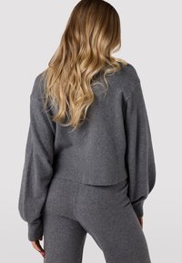 Maglione grigio corto con maniche lunghe a sbuffo, orlo a coste e texture morbida. Abbinato a pantaloni grigi aderenti coordinati.