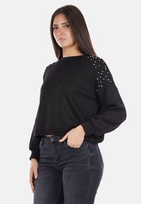 Maglione nero cropped realizzato in morbido tessuto, con spalle impreziosite da piccoli borchie. Maniche lunghe e scollatura rotonda.
