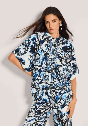 Bloemenblouse met korte mouwen, met blauw-zwarte patronen op een witte achtergrond. Ruches aan de voorkant, lichtgewicht materiaal.