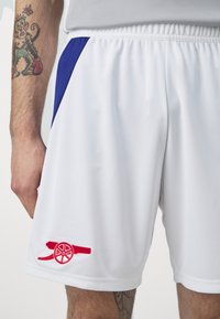 Pantalones cortos deportivos blancos con acentos laterales azules y un logo bordado rojo, que cuentan con una cinturilla elástica y una tela ligera y suave.