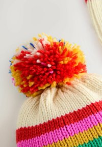 Knitted beanie in cream with multicolored horizontal stripes (red, pink, yellow, green) and a fluffy multicolored pom-pom on top.