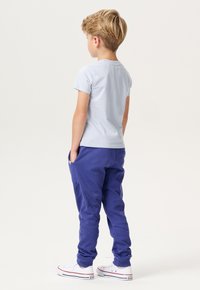 Lichtblauwe T-shirt met korte mouwen in combinatie met paarse joggingsbroek, met een relaxte pasvorm en witte sneaker met rode accenten.