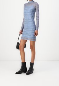 Robe bleu transparente à manches longues avec un motif répété du logo "HUGO". Elle se caractérise par un col haut et une coupe ajustée. Associe avec des bottines noires et un sac.