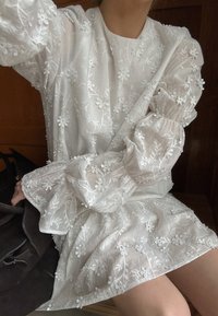 Balta siuvinėta suknel�ė su gėlių raštais ir pūstomis rankovėmis, pagaminta iš lengvos medžiagos su tekstūriniais apdailos elementais.