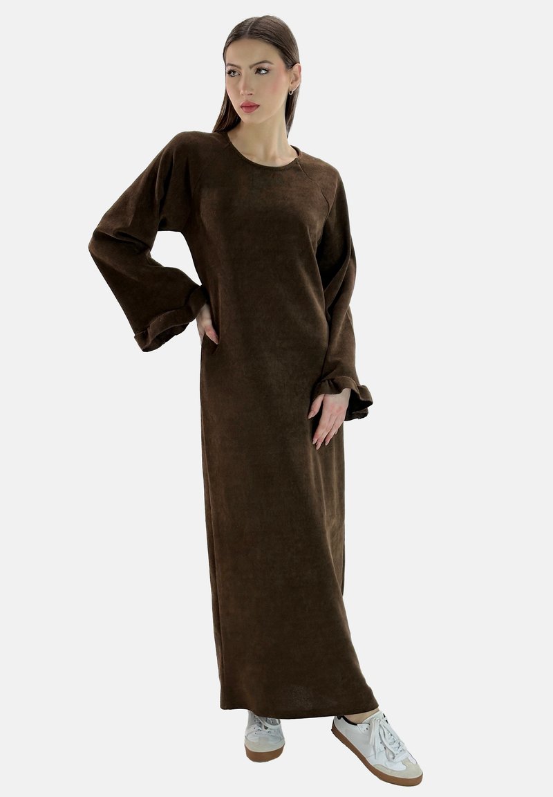 Vestido maxi marrón de manga larga hecho de una tela suave; cuenta con mangas anchas y se lleva con zapatillas blancas; diseño simple y relajado.