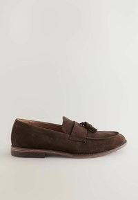 Mocasines de gamuza marrón con puntera redondeada, detalle decorativo de borlas y suela de cuero en contraste. Textura suave y elegancia casual.