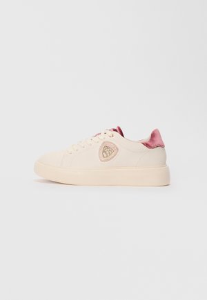 Baskets crèmes avec semelle épaisse, languette en velours rose à l'arrière, système de laçage sur le devant et logo en forme de bouclier avec accents dorés sur le côté.