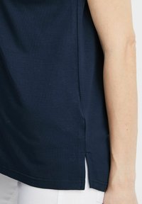 Maglietta in cotone blu navy con vestibilità rilassata, fenditure laterali e maniche corte. Tessuto liscio con leggere imperfezioni visibili.