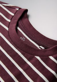 Prim-plan cu un tricou bordo cu dungi albe și guler rotund, cusături vizibile și textură a țesăturii.