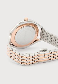 Κοντινό πλάνο σε δίχρωμο μεταλλικό ρολόι με μπρασελέ από ανοξείδωτο ατσάλι και ροζ χρυσό, εμφανίζοντας την πίσω θήκη και τις λεπτομέρειες της πόρπης.