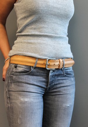 Hellbrauner Ledergürtel mit silberner Schnalle, getragen über einem grauen, gerippten Tanktop und gewaschenen grauen Jeans. Einfaches Design, strukturiertes Leder.