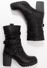 Botas de tobillo de cuero sintético negro con tacón robusto, caña arrugada, detalles de hebilla y cremallera lateral, con suela acanalada para mayor agarre.