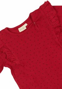 Piros kötött felső, melyet kisebb fekete pöttyök díszítenek, fodros ujjakkal és kerek neckline-nal. A címke jól látható, rajta a "petit pîa" márkanevével.