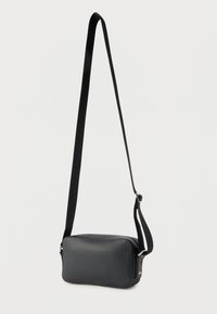 Μαύρη τσάντα crossbody με υφή, ρυθμιζόμενο λουρί, ορθογώνιο σχήμα και ασημί φερμουάρ σε απλό λευκό φόντο.