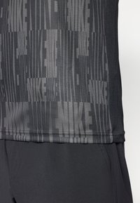 Camiseta deportiva negra con un diseño en patrón en diferentes tonos de gris, mostrando de manera prominente la palabra "NIKE" en múltiples ubicaciones y texturas.