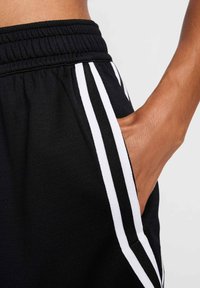 Black joggers featuring white side stripes, elastic waistband, and a side pocket. Close-up view emphasizing fabric texture and design details.
