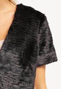 Gilet in finta pelliccia nera con superficie testurizzata e a coste. Design aperto davanti con maniche corte, che enfatizza morbidezza e calore.