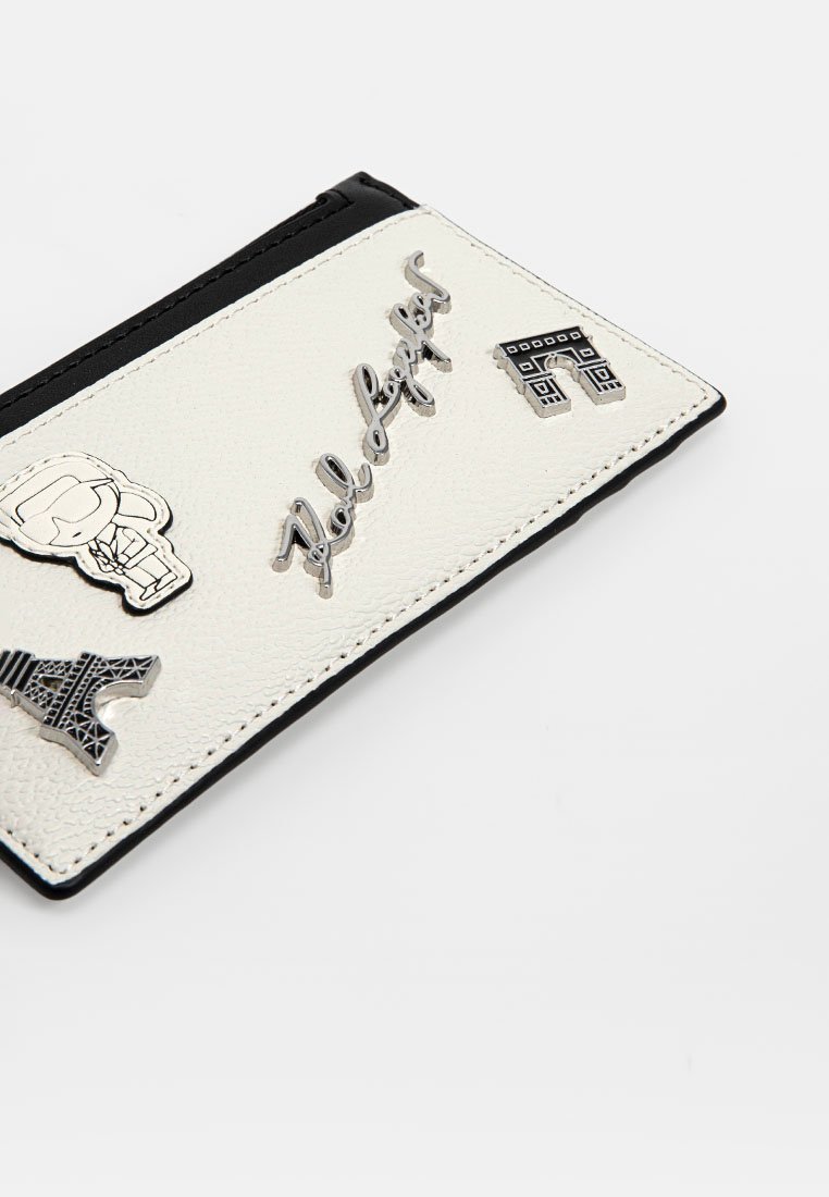 Weiße Lederkarteihülle mit schwarzen Akzenten, ausgestattet mit silberfarbener Hardware und grafischen Designs, darunter ein Totenkopf, der Eiffelturm und Text.