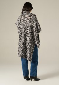 Poncho lavorato a maglia in bianco e nero, con colletto alto, vestibilità ampia e motivo testurizzato. Abbinato a jeans blu e stivaletti alla caviglia.