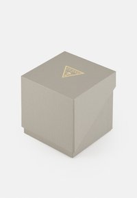 Grå teksturert pappeske med en triangel-formet gulllogo på toppen. Lokkets design er litt skrå.