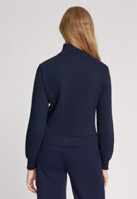 Pullover blu navy con colletto alto, polsini e orlo a costine, realizzato in tessuto morbido con un design aderente e texture liscia.