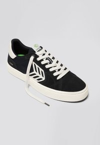 Schwarze Wildleder-Sneaker mit weißer Gummisohle, ausgestattet mit einem Blattdesign an der Seite, weißen Schnürsenkeln und einem grünen Akzent auf der Zunge.