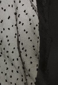 Black mesh fabric with scattered black dots, layered with a black textured material. The design features ruffled edges for added detail.