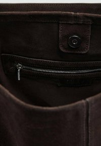 Interior de bolso en ante marrón que cuenta con un bolsillo con cremallera y cierre a presión. Acabado texturizado y suave con un diseño limpio.