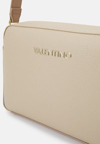 Beige leren handtas met gouden "VALENTINO" logo, rechthoekige vorm, gestructureerd oppervlak en een contrasterende bruine band.