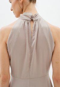 Helles taupe-farbenes ärmelloses Kleid mit hohem Kragen, das über ein knöpfbares Rückendetail und einen weichen, strukturierten Stoff verfügt. Saubere und elegante Silhouette.
