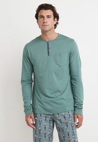 Langarm, teal henley shirt met een knoopsluiting van drie knopen, ronde halslijn en een borstzak; gecombineerd met gestreepte pyjamabroek.