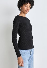 Top negru cu mâneci lungi, cu un model texturat. Materialul pare moale și elastic, asortat cu blugi denim de un albastru deschis.