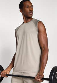 Μπεζ αμάνικο αθλητικό μπλουζάκι από λεία ύφανση, με στρογγυλή λαιμόκοψη και ραφές flatlock, φορεμένο από άτομο που κρατάει μια μπάρα με βάρη.