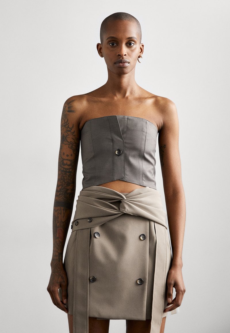 Top corto grigio senza spalline con design strutturato e dettagli con bottoni frontali, abbinato a una gonna beige a vita alta con tessuto attorcigliato e bottoni.