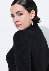 Zwarte ribbel turtleneck trui met lange mouwen. Zachte textuur en aansluitende pasvorm. Accessoires met grote zilveren hoepeloorbellen.