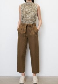 Pantalons taille haute en papier brun avec plis, associés à un haut sans manches texturé crème et marron. Portés avec des chaussures chunky de couleur claire.
