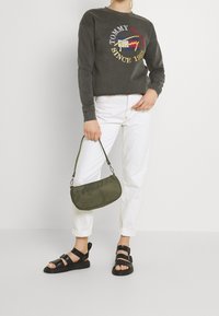 Tmavě šedá mikina s logem, bílé džíny, zelená kabelka přes rameno a černé sandály se šňůrkami. Neformální outfit s různými texturami.