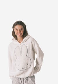 Biała, pluszowa bluza z kapturem z dużą szarą grafiką królika na przodzie. Posiada sznurki do regulacji na kapturze i luźny krój. W zestawie ze wzorzystymi szarymi spodniami.