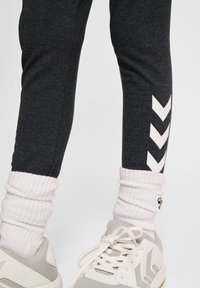 Szare legginsy sportowe z białym wzorem w zygzak po boku, w komplecie z prążkowanymi białymi skarpetkami i jasnoszarymi butami sportowymi.