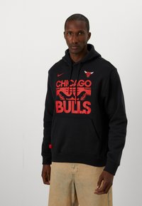 Felpa nera con cappuccio in cotone, dotata di tasca a marsupio. Presenta il testo rosso "CHICAGO BULLS" e il logo sul petto, con il simbolo Nike sopra.