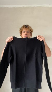 Zwarte gebreide trui met een hoge kraag en een rits aan de voorkant, voorzien van lange mouwen en een gestructureerde afwerking.