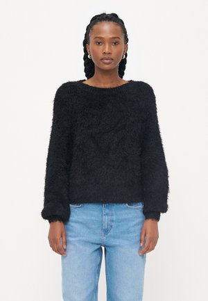 Zwarte fuzzy trui met een ronde halslijn en lange mouwen, met een zachte textuur en een relaxte pasvorm. Gepaard met lichtblauwe jeans.