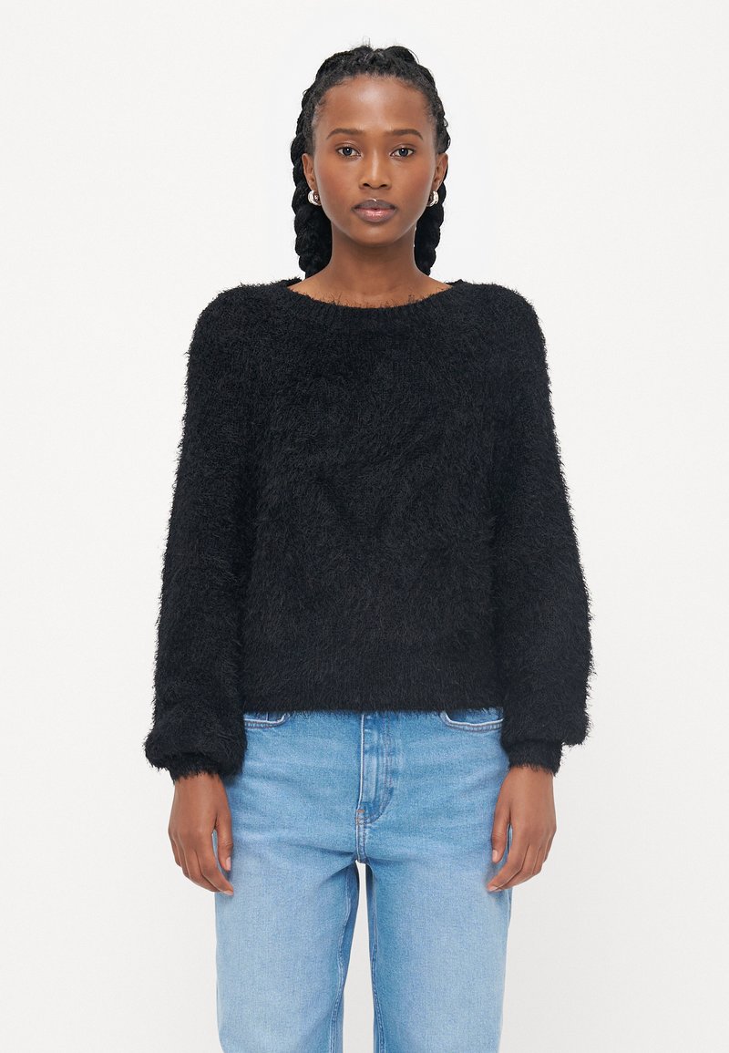 Zwarte fuzzy trui met een ronde halslijn en lange mouwen, met een zachte textuur en een relaxte pasvorm. Gepaard met lichtblauwe jeans.
