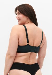 Dark green bra with adjustable straps and hook closure. Smooth fabric with a seamless back design. Paired with black lace-trimmed underwear.