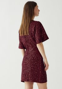 Bordo suknelė trumpomis rankovėmis, padengta blizgučiais, su prigludusia siluetu ir užtrauktuku nugaroje. Lygi tekstūra, iki kelių ilgio.